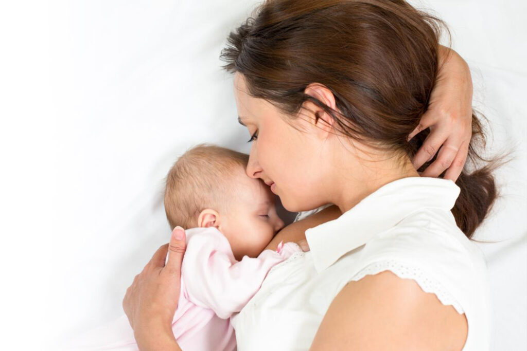 Madre con bebé en la cama. Madre apoyando los labios sobre la cabeza de su bebé